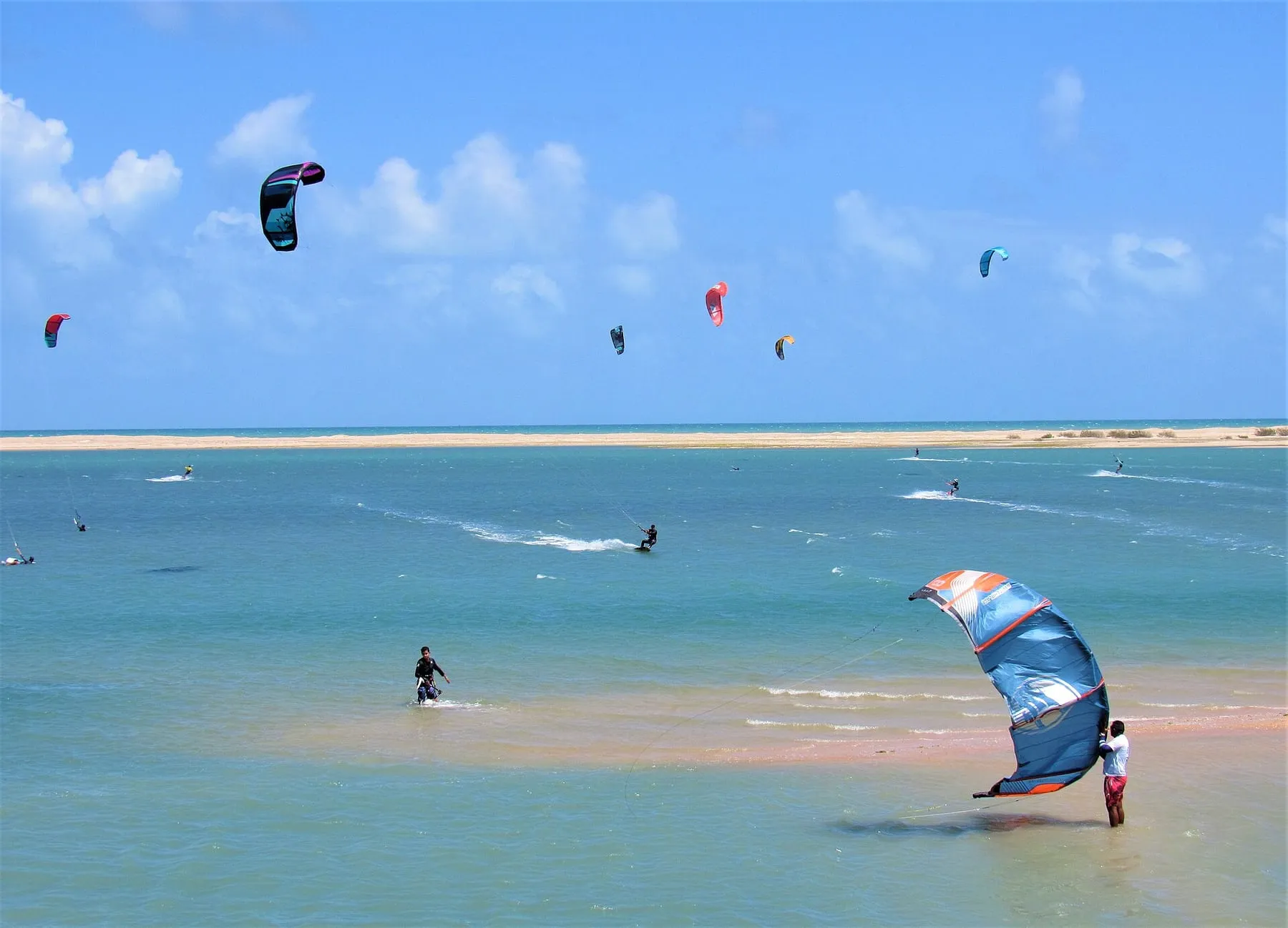 Kitesurfistas velejando na água azul e rasa da Ilha do Guajiru, no Ceará